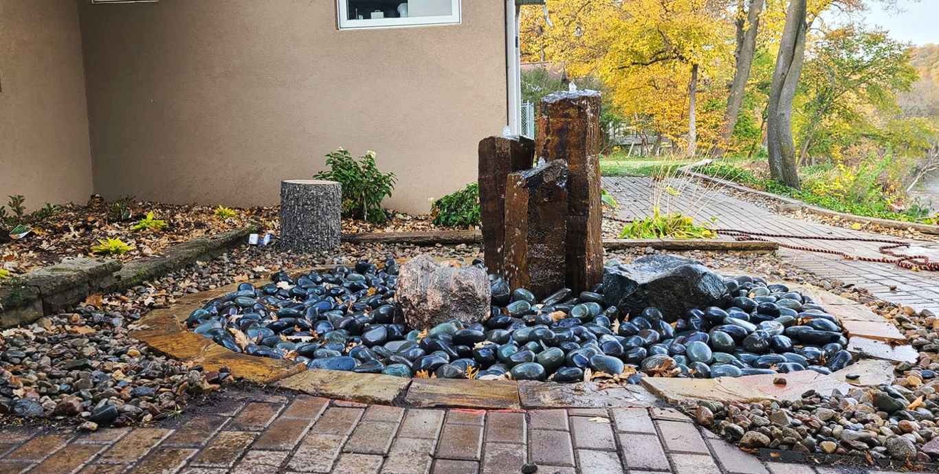 Basalt column fountainscape set in dark river rock beside a paver patio