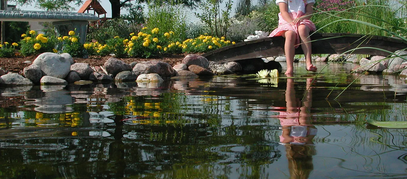 Person sitting on a stone bridge dipping their feet into a repaired pond